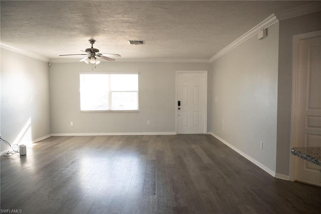 Unfurnished living room with dark wood-style floors, a textured ceiling, crown molding, and a ceiling fan