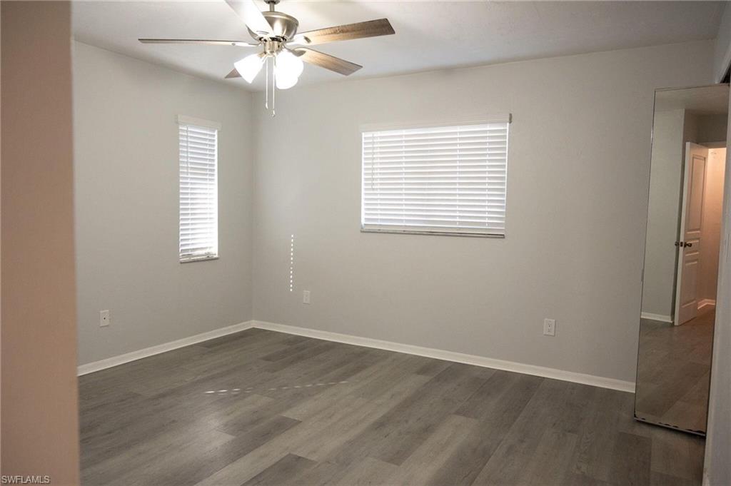 Unfurnished room with dark wood-style floors, healthy amount of natural light, and ceiling fan