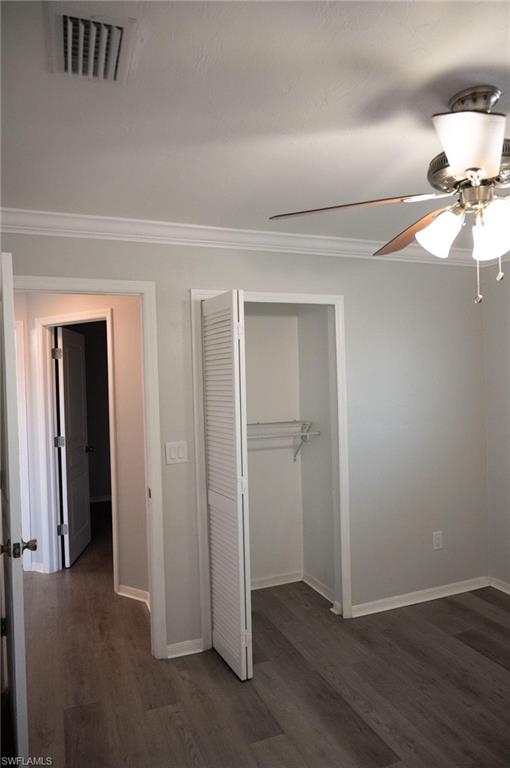Unfurnished bedroom featuring dark wood finished floors, a closet, ornamental molding, and a ceiling fan