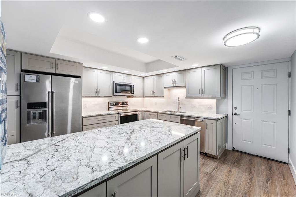 Beautiful Kitchen featuring gray cabinetry, a raised ceiling, stainless steel appliances, light stone countertops, and recessed lighting
