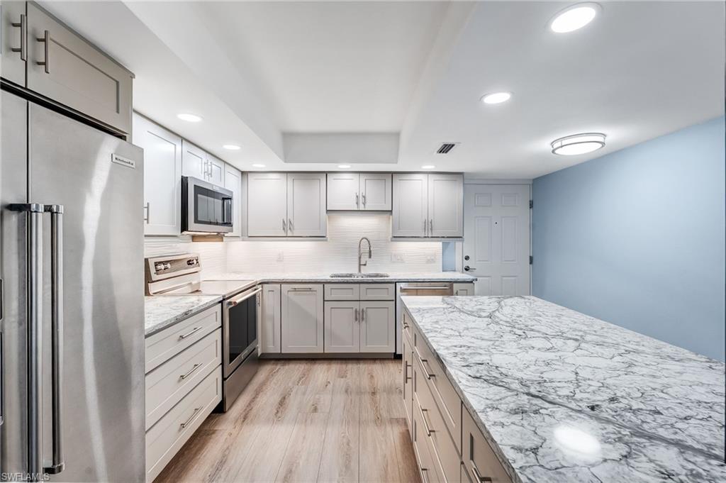 Kitchen featuring  lots of cabinets and drawer!  a dream kitchen with appliances with stainless steel finishes, recessed lighting, light stone countertops, light wood finished floors, and gray cabinetry
