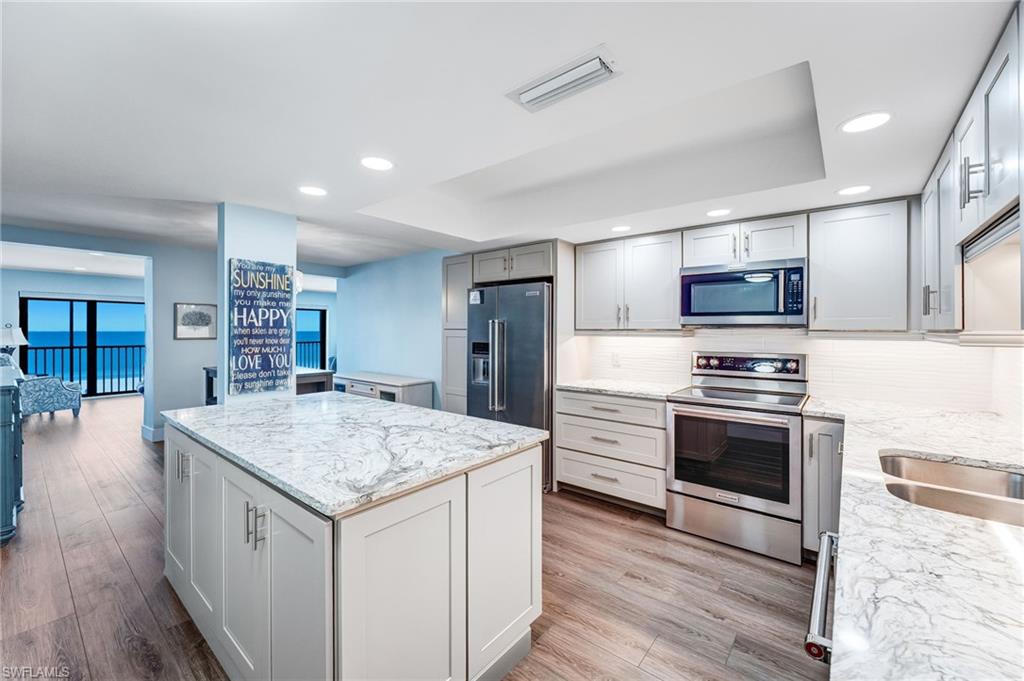 Spacious Kitchen featuring stainless steel appliances, recessed lighting, a tray ceiling, light stone counters, and a center island