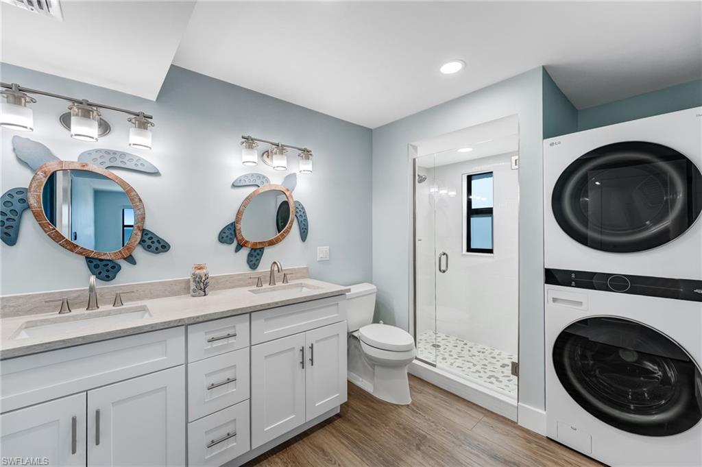 Master Bathroom with double vanity, light wood finished floors, stacked washer and clothes dryer, a stall shower, and recessed lighting