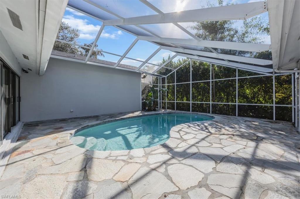 Outdoor pool featuring a sunroom, a patio area, and glass enclosure
