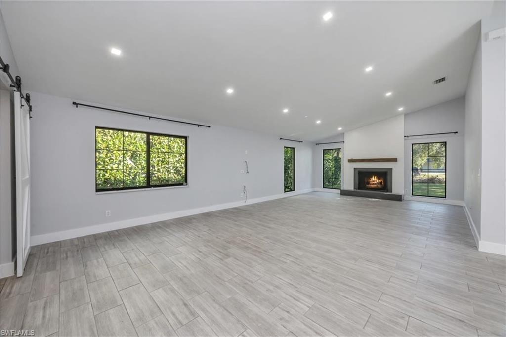 Unfurnished living room with a barn door, recessed lighting, a warm lit fireplace, lofted ceiling, and wood finish floors
