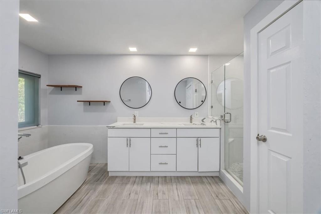 Bathroom with a stall shower, a freestanding bath, double vanity, wainscoting, and wood finish floors
