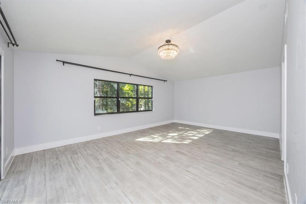 Empty room with lofted ceiling, light wood-style floors, and a chandelier