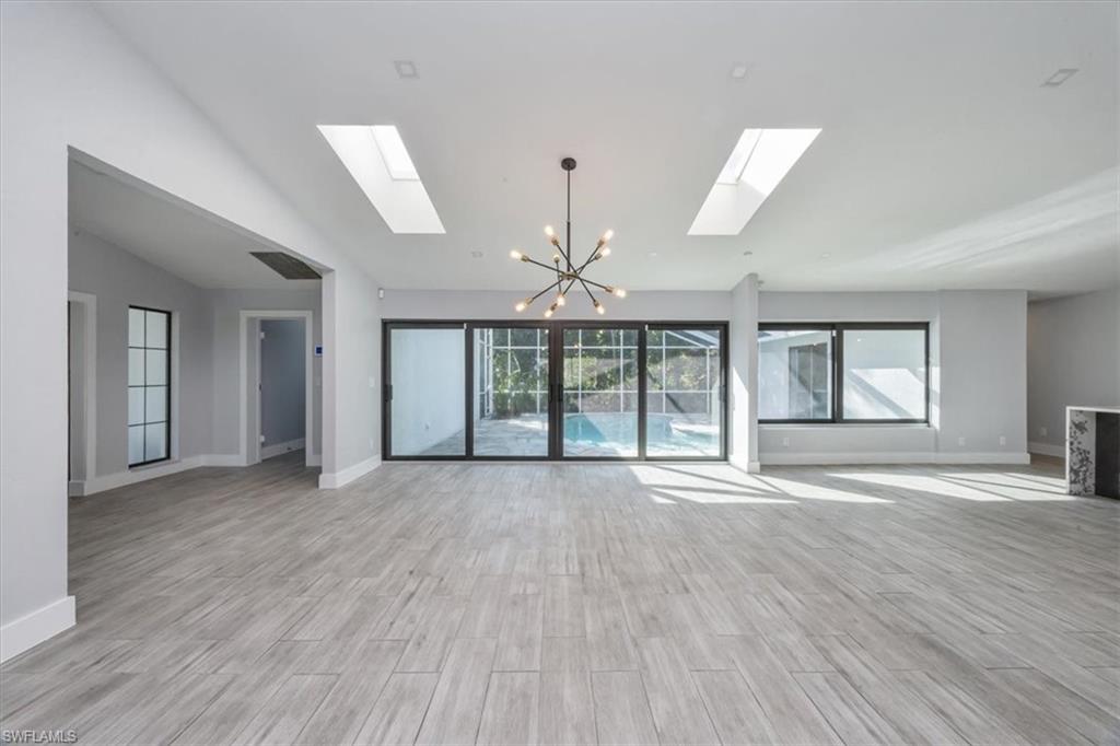 Unfurnished living room with a chandelier, wood finish floors, lofted ceiling, and a skylight