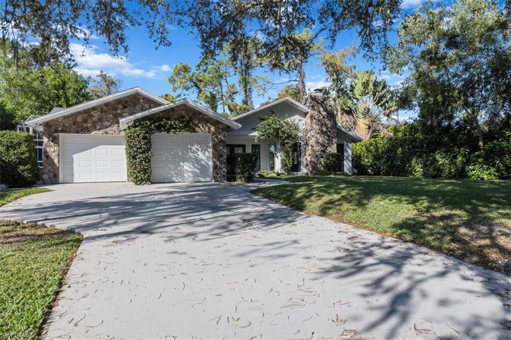 View of front facade with stone siding, a front yard, concrete driveway, and a garage