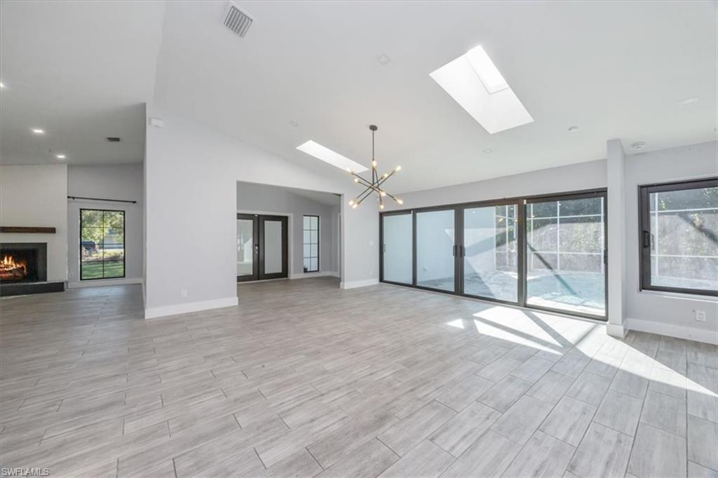 Unfurnished living room with a chandelier, a lit fireplace, a skylight, wood finish floors, and high vaulted ceiling