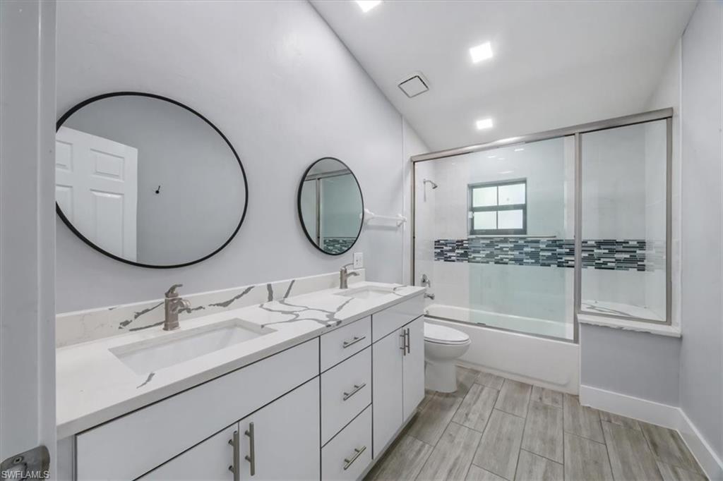 Bathroom featuring bath / shower combo with glass door, double vanity, and wood finish floors