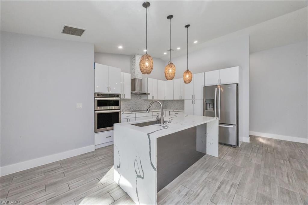Kitchen with appliances with stainless steel finishes, decorative light fixtures, white cabinets, an island with sink, and light stone countertops