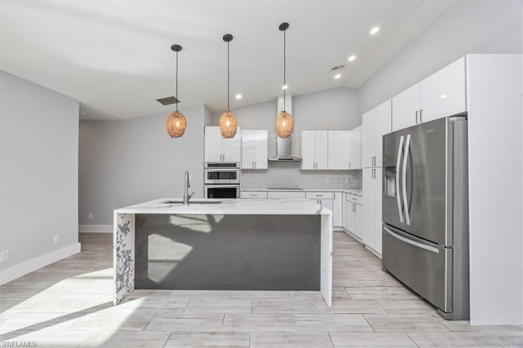 Kitchen featuring stainless steel appliances, decorative light fixtures, light stone counters, vaulted ceiling, and white cabinets