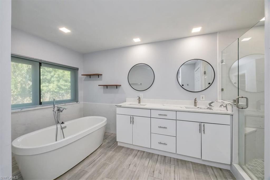 Full bath featuring double vanity, a freestanding tub, wainscoting, a stall shower, and wood tiled floors