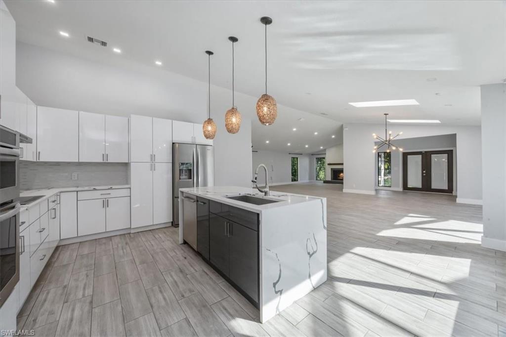 Kitchen featuring decorative light fixtures, vaulted ceiling, a chandelier, white cabinets, and a kitchen island with sink