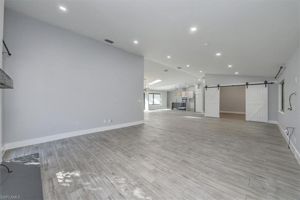 Unfurnished living room featuring a barn door, recessed lighting, wood tiled floors, and lofted ceiling