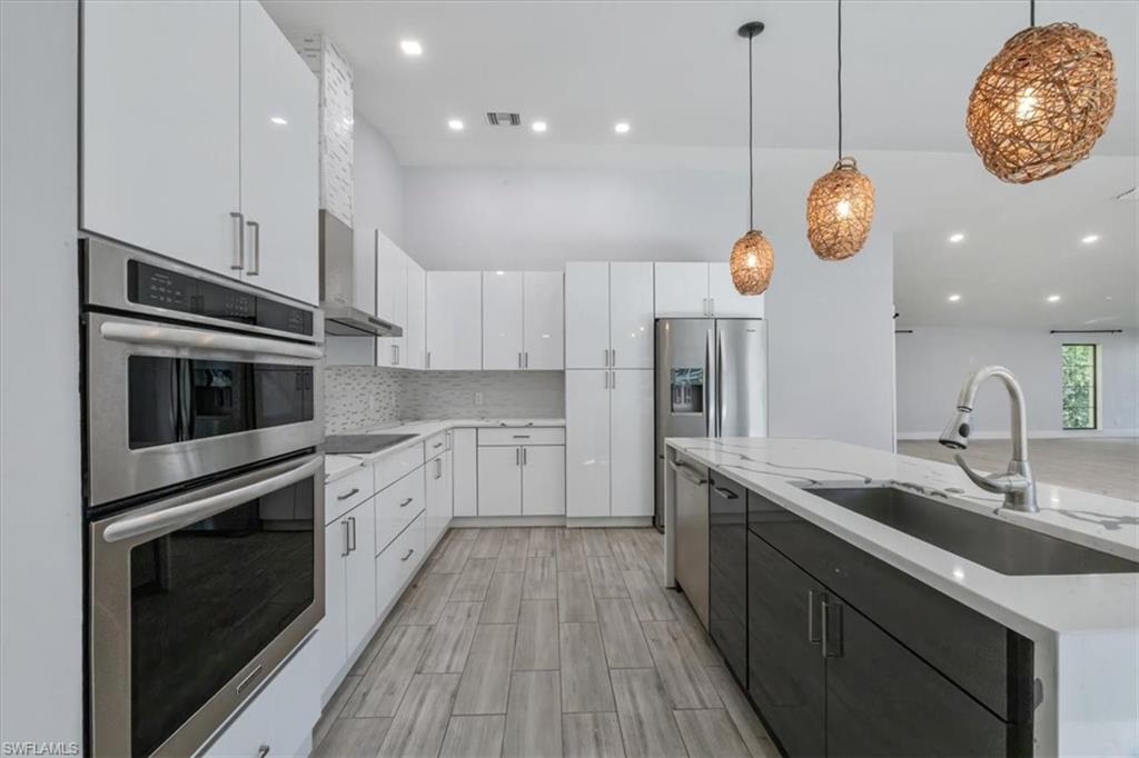Kitchen with stainless steel appliances, white cabinetry, hanging light fixtures, a kitchen island with sink, and recessed lighting