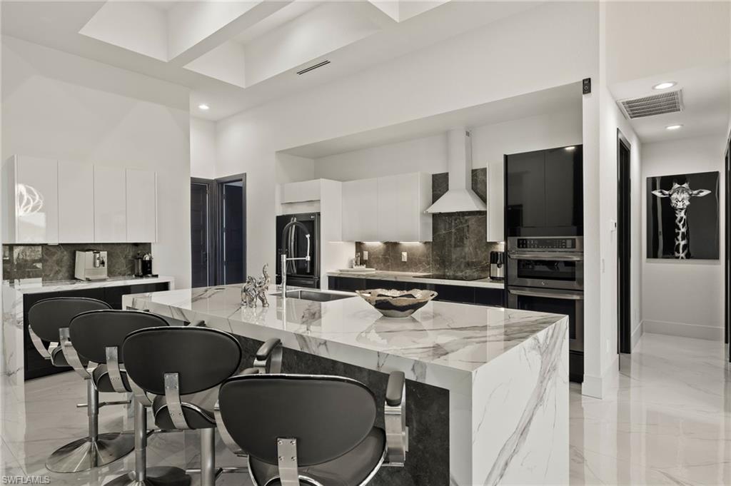 Kitchen featuring white cabinets, modern cabinets, a breakfast bar area, light stone countertops, and recessed lighting