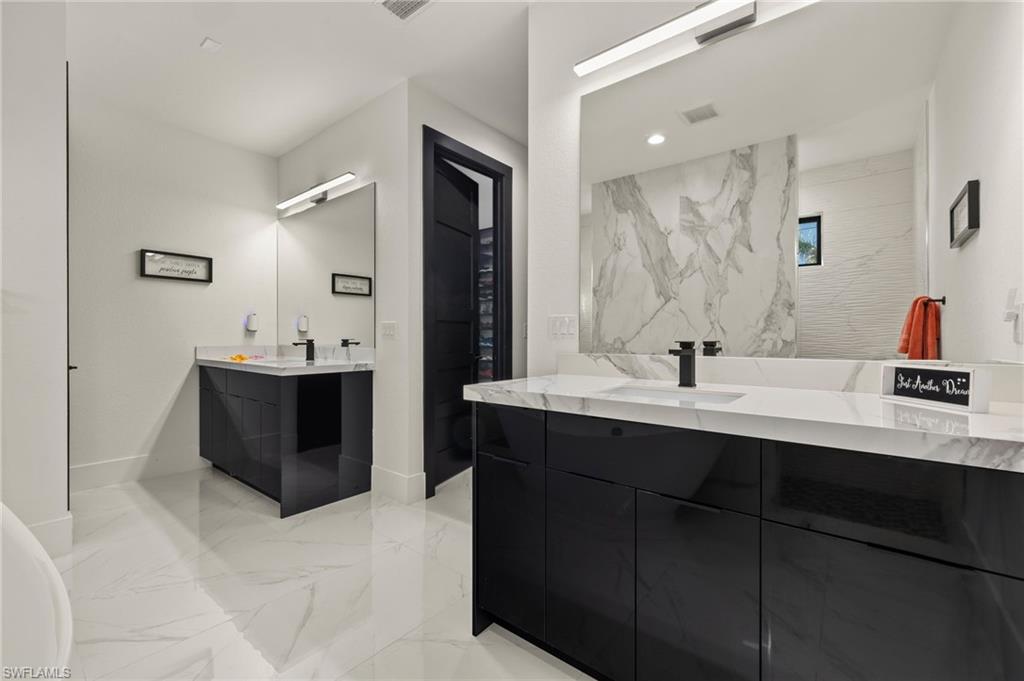 Full bath with light marble finish floors and two vanities