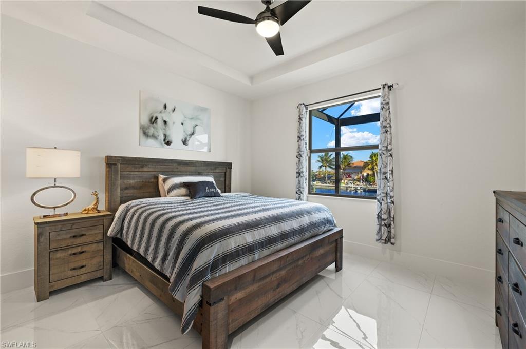 Bedroom featuring a tray ceiling, a ceiling fan, and light marble finish flooring
