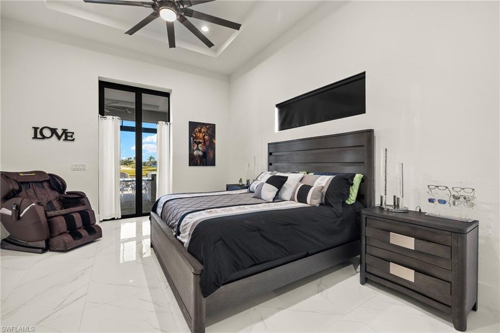 Bedroom with marble tiled flooring, access to exterior, a raised ceiling, ceiling fan, and a towering ceiling