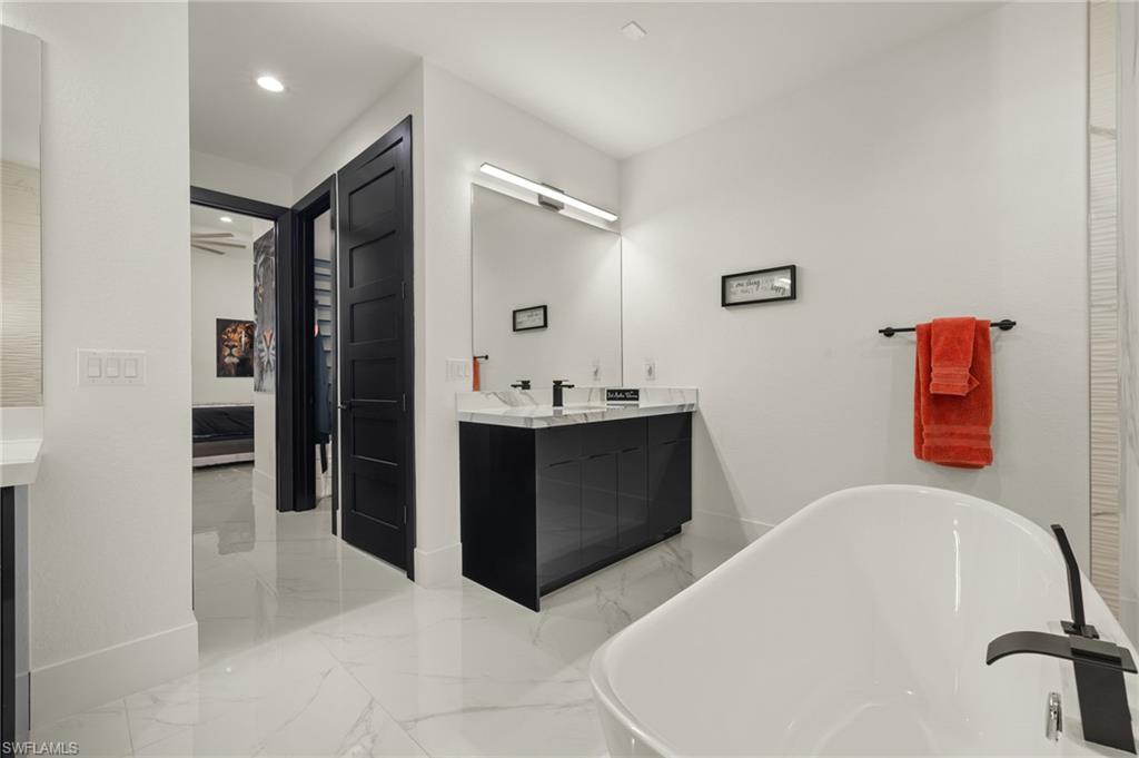 Ensuite bathroom featuring vanity, a soaking tub, light marble finish flooring, and recessed lighting