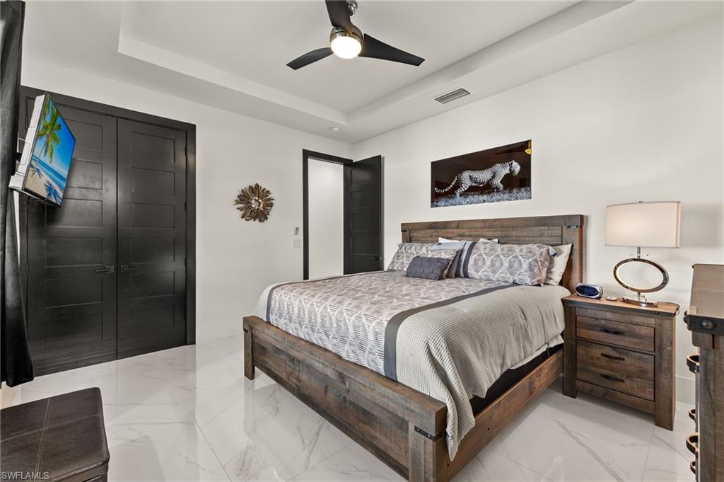 Bedroom with light marble finish flooring, a tray ceiling, and a ceiling fan