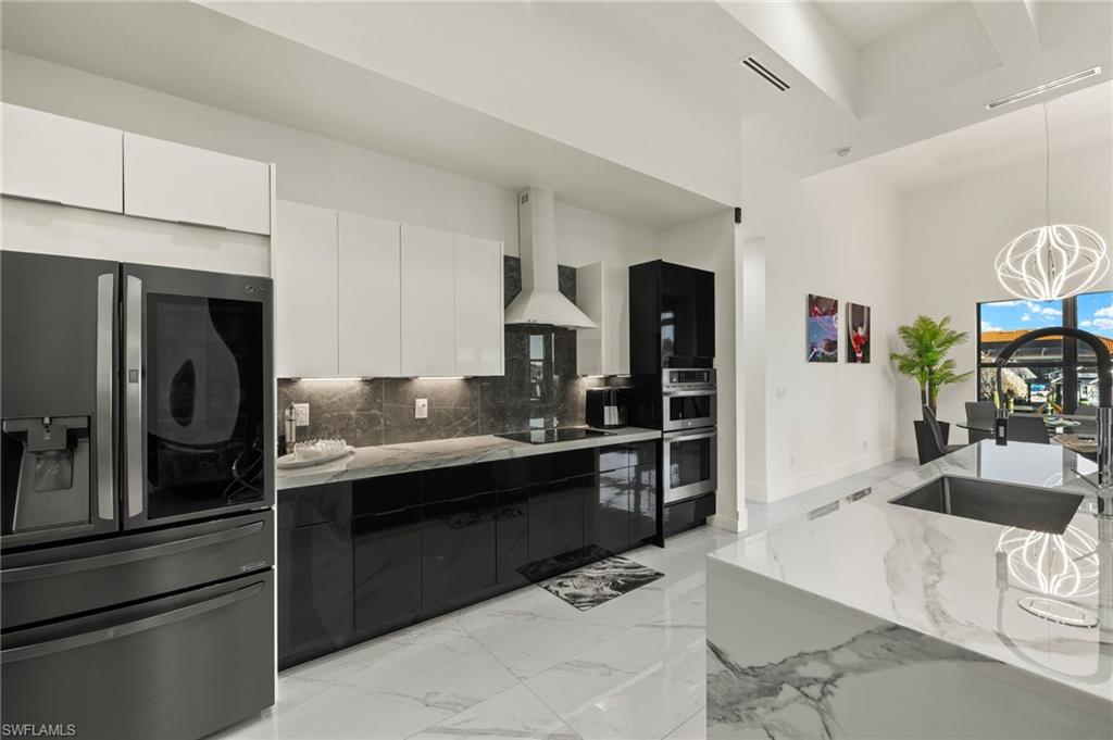 Kitchen with appliances with stainless steel finishes, modern cabinets, white cabinetry, dark cabinets, and wall chimney range hood