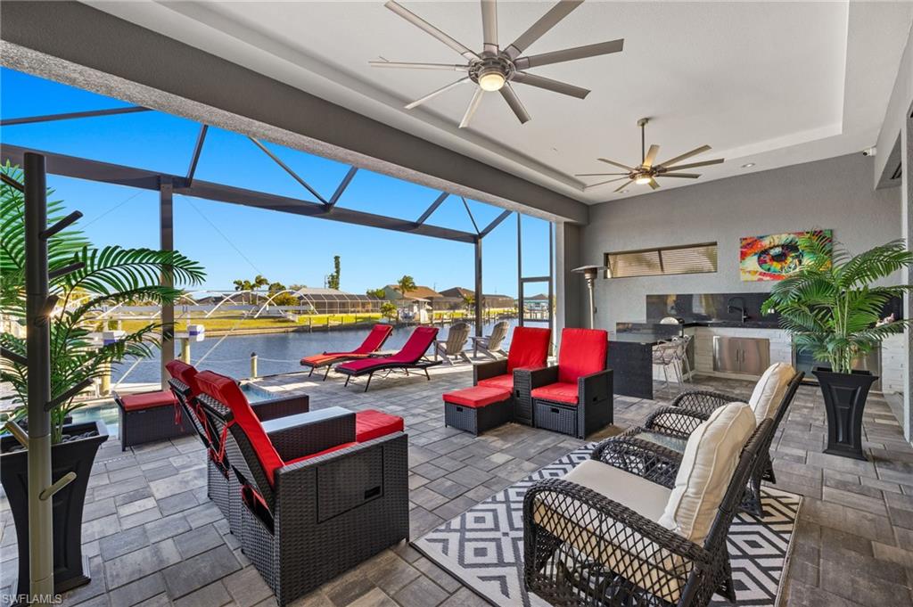 View of patio / terrace featuring a water view, a lanai, a sunroom, an outdoor hangout area, and an outdoor kitchen