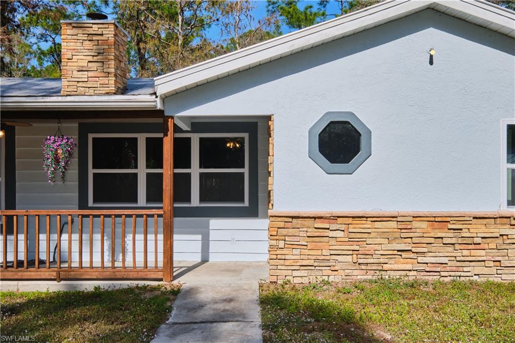 View of exterior entry featuring covered porch, a chimney, and stucco siding