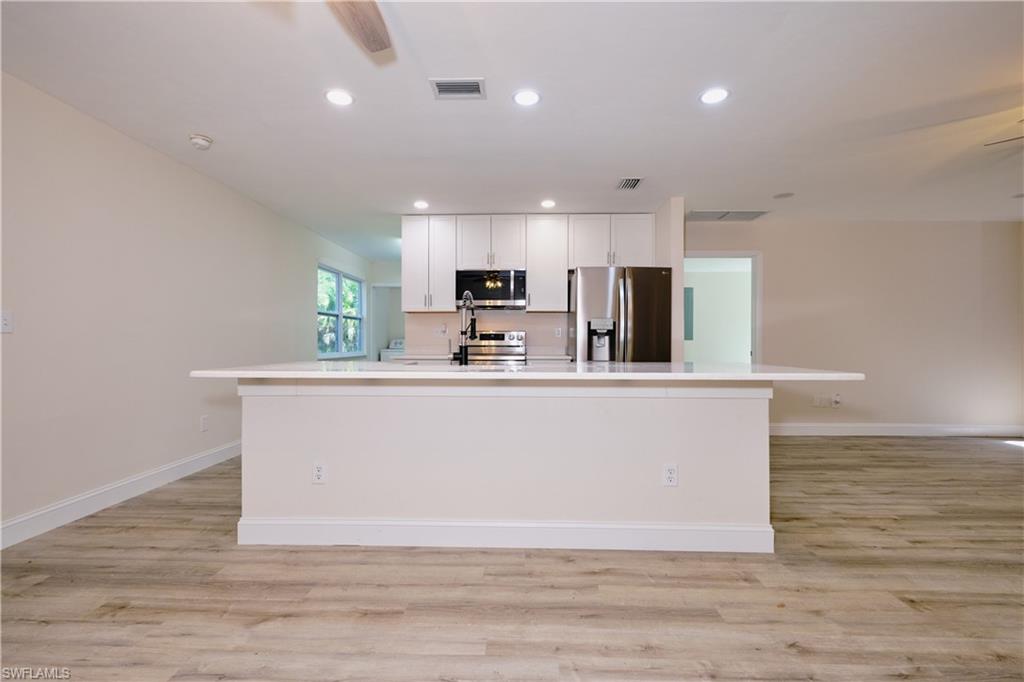 Kitchen with appliances with stainless steel finishes, a center island with sink, white cabinets, light wood finished floors, and recessed lighting