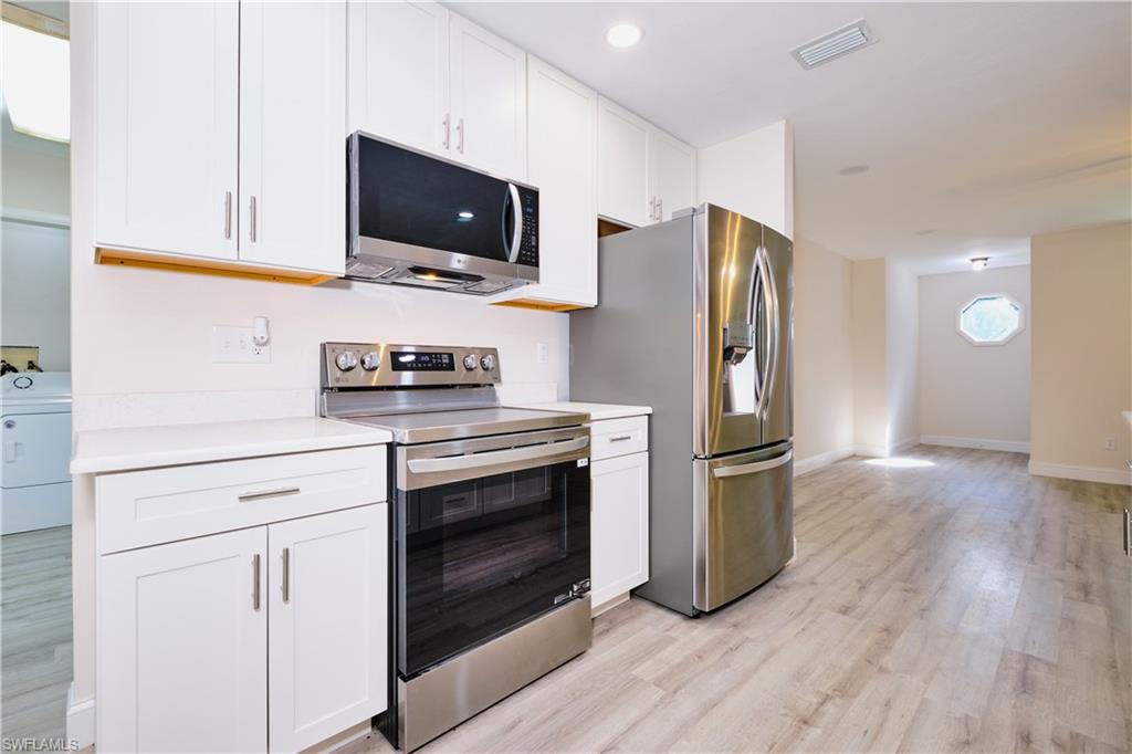 Kitchen with appliances with stainless steel finishes, white cabinetry, light countertops, and washer / clothes dryer