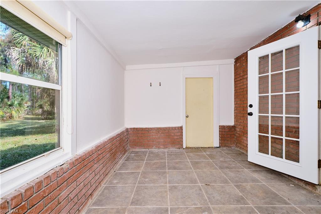 Unfurnished sunroom with brick wall, a wainscoted wall, and lofted ceiling