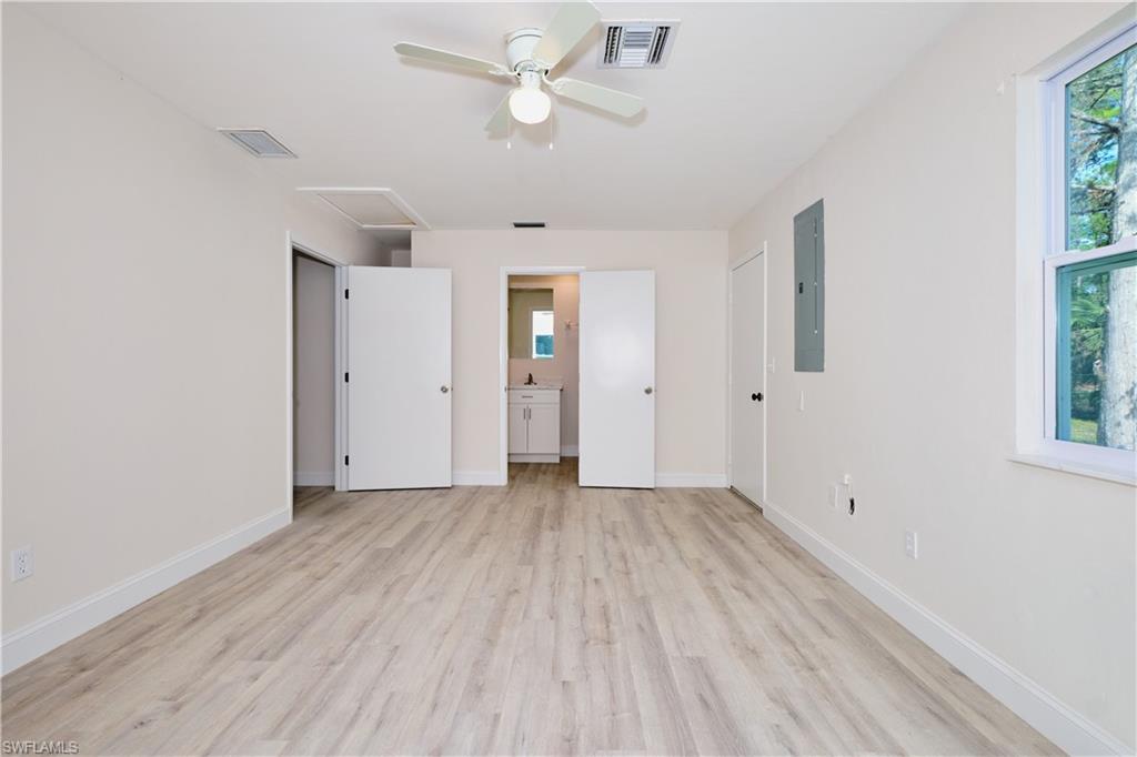 Unfurnished bedroom with connected bathroom, multiple windows, attic access, and light wood-style flooring