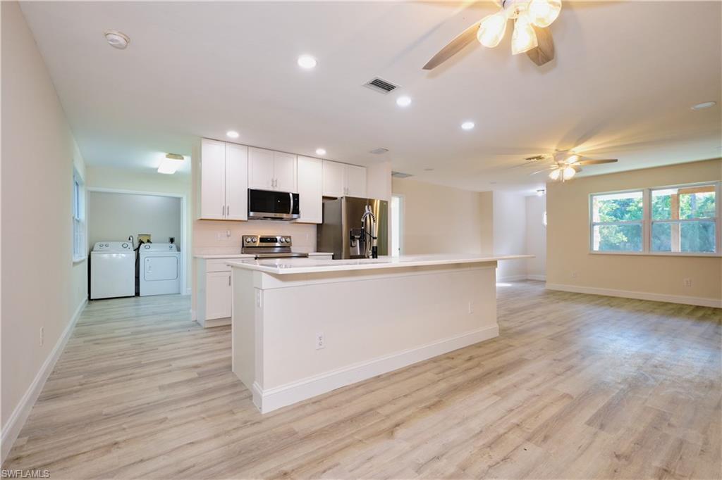 Kitchen featuring healthy amount of natural light, washing machine and dryer, white cabinets, and recessed lighting