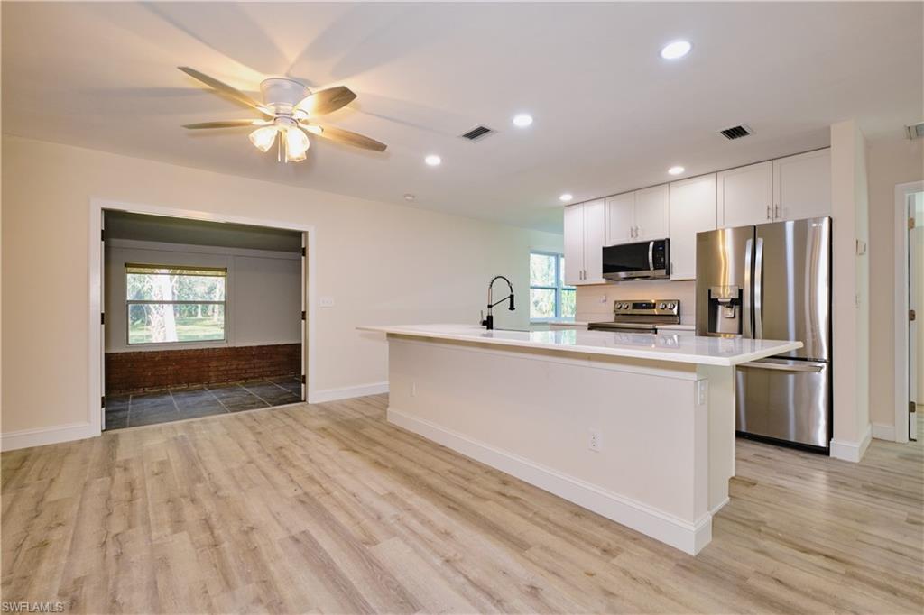 Kitchen featuring appliances with stainless steel finishes, a kitchen island with sink, white cabinets, light wood-style floors, and recessed lighting