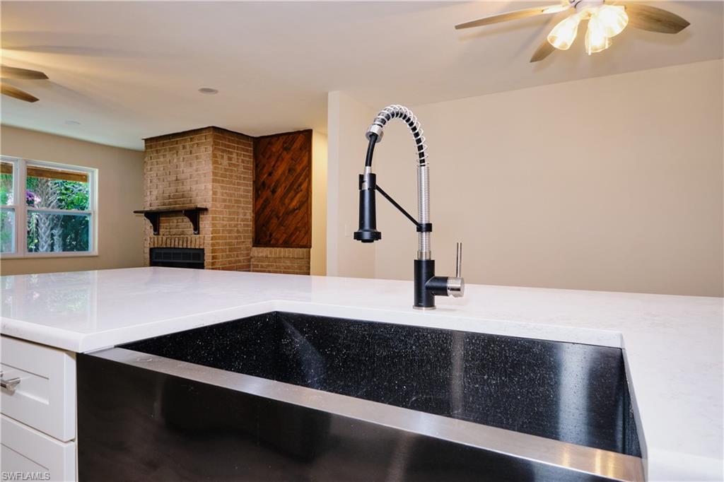 Kitchen view of a ceiling fan, a brick fireplace, light stone countertops, and white cabinets