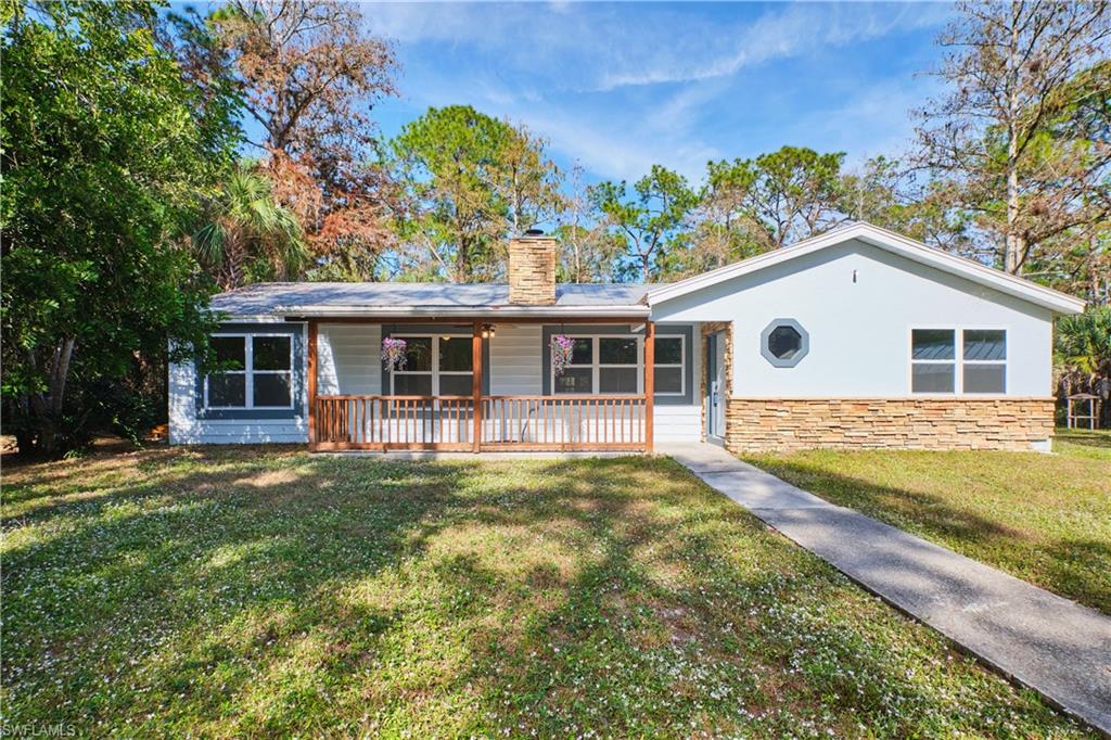 Ranch-style house featuring a front lawn, a chimney, stucco siding, a porch, and stone siding