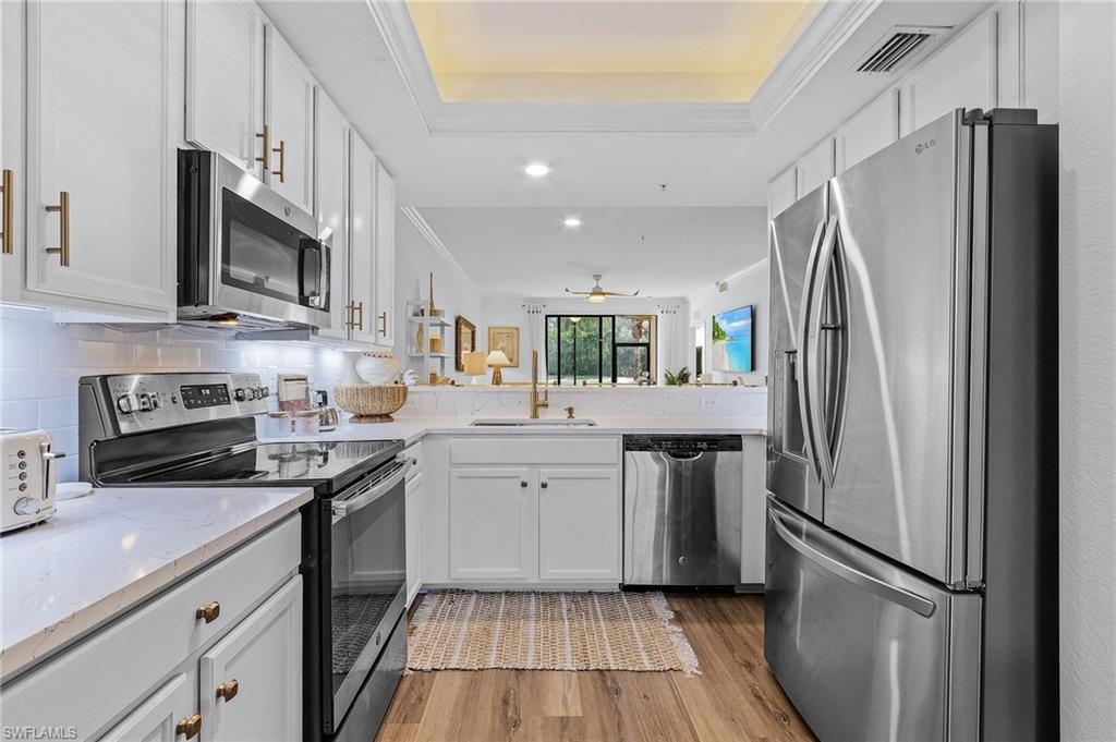 Kitchen featuring sink, light wood-type flooring, appliances with stainless steel finishes, tasteful backsplash, and white cabinetry