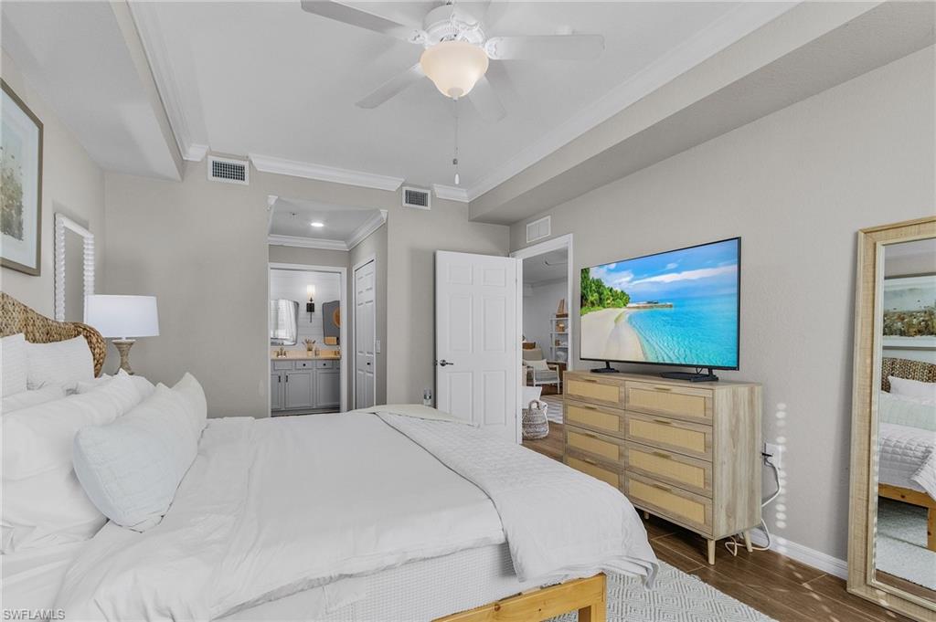 Bedroom with ensuite bathroom, ceiling fan, ornamental molding, and dark wood-type flooring