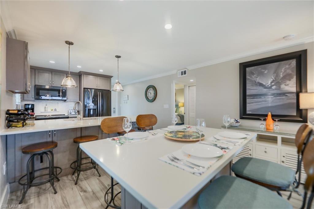 Kitchen featuring a kitchen breakfast bar, gray cabinetry, appliances with stainless steel finishes, a peninsula, and ornamental molding