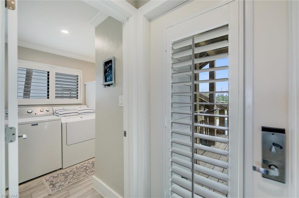 Washroom with ornamental molding, washing machine and clothes dryer, and light wood-style flooring