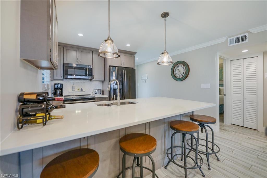 Kitchen featuring a peninsula, stainless steel appliances, a breakfast bar, decorative light fixtures, and light stone counters