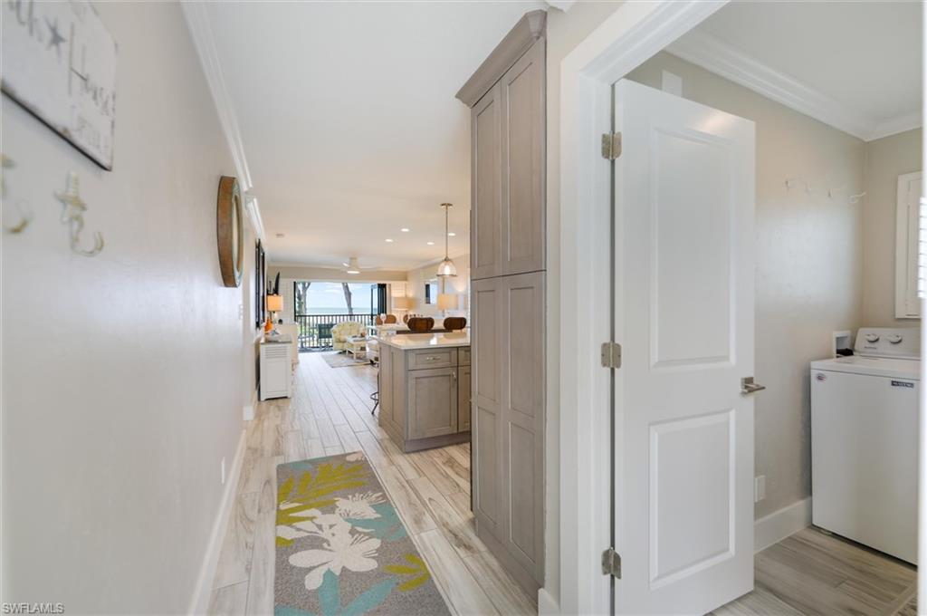 Hall with washer / dryer, wood finish floors, and ornamental molding