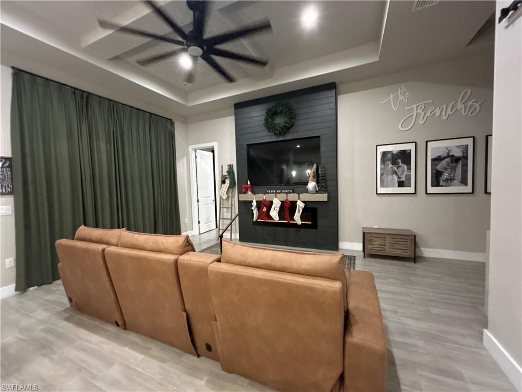 Living room with a tray ceiling, ceiling fan, a large fireplace, and light wood-style floors
