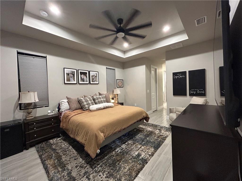 Bedroom featuring a raised ceiling, a ceiling fan, light wood-type flooring, and recessed lighting