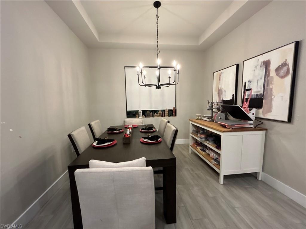 Dining area with a tray ceiling, light wood-style floors, and a chandelier