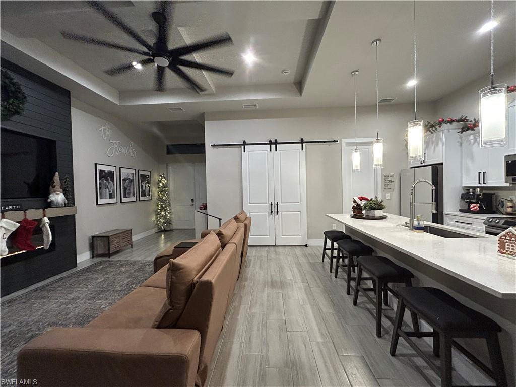 Living room featuring a barn door, a raised ceiling, wood finish floors, ceiling fan, and recessed lighting