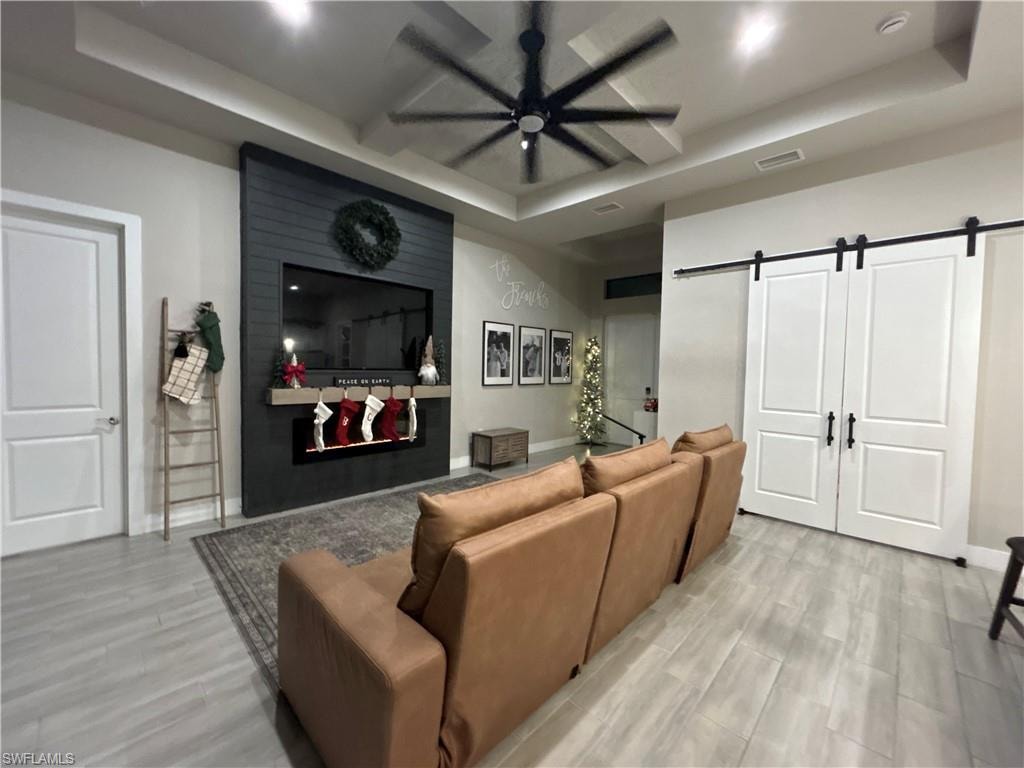 Living room featuring a barn door, a tray ceiling, a ceiling fan, light wood-type flooring, and a large fireplace
