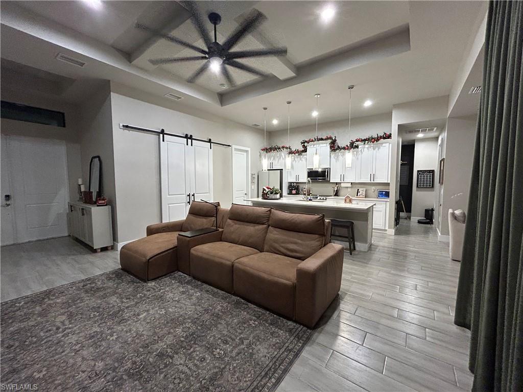 Living area with a barn door, a raised ceiling, wood tiled floors, a ceiling fan, and recessed lighting
